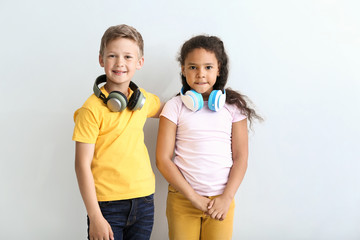 Cute little children with headphones on light background