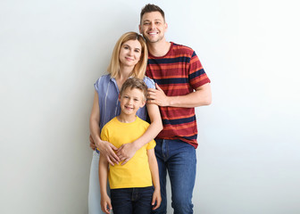 Happy couple with little adopted boy on light background