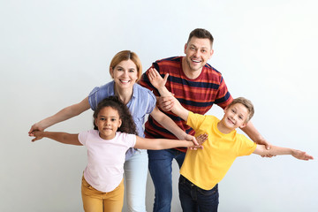 Happy couple with little adopted children on light background