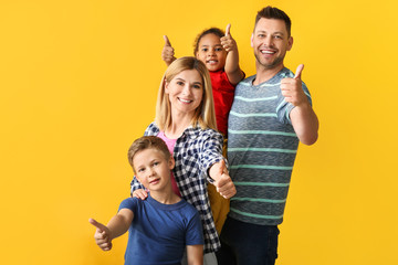 Happy couple with little adopted children showing thumb-up on color background