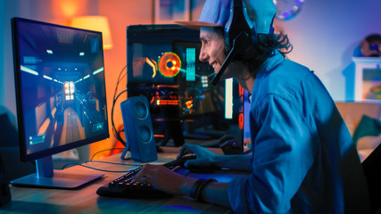 Professional Gamer Playing First-Person Shooter Online Video Game on His Powerful Personal Computer. Room and PC have Colorful Neon Led Lights. Young Man is Wearing a Cap. Cozy Evening at Home.