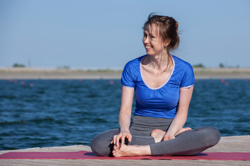 Young woman exercising yoga pose by the lake shore at sunset, girl in headstand yoga pose. People...