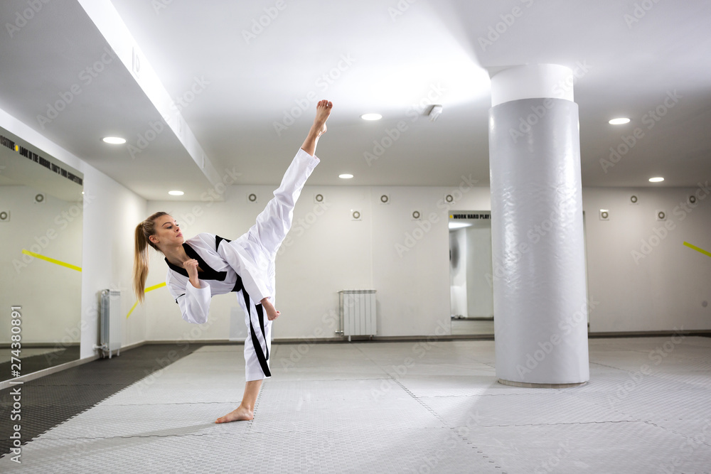 Wall mural Cute girl with dyed blonde hair practicing martial art of taekwondo