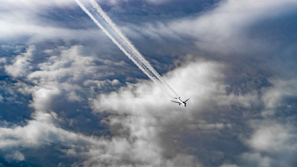Luftaufnahme auf ein unter uns fliegendes Flugzeug mit Kondensstreifen