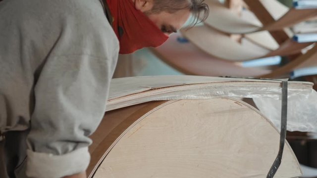Worker glues veneer on a wooden part apt glue press machine plywood workshop factory. Craftman man equipment