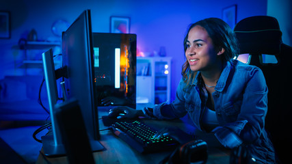 Beautiful and Excited Black Gamer Girl is Playing First-Person Shooter Online Video Game on Her Computer. Room and PC have Blue Neon Led Lights. Cozy Evening at Home. © Gorodenkoff