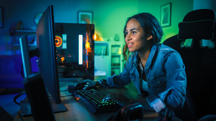 Beautiful and Excited Black Gamer Girl is Playing First-Person Shooter Online Video Game on Her Computer. Room and PC have GreenNeon Led Lights. Cozy Evening at Home. - obrazy, fototapety, plakaty