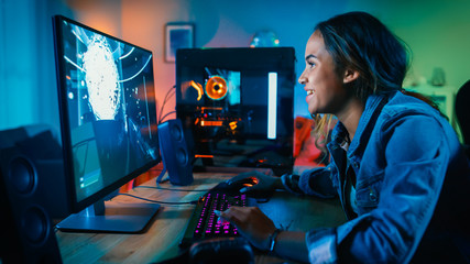 Beautiful and Excited Black Gamer Girl is Playing First-Person Shooter Online Video Game on Her Computer. Room and PC have GreenNeon Led Lights. Cozy Evening at Home.