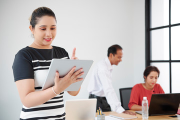 Young Asian businesswoman standing and using digital tablet with business people working in team in the background