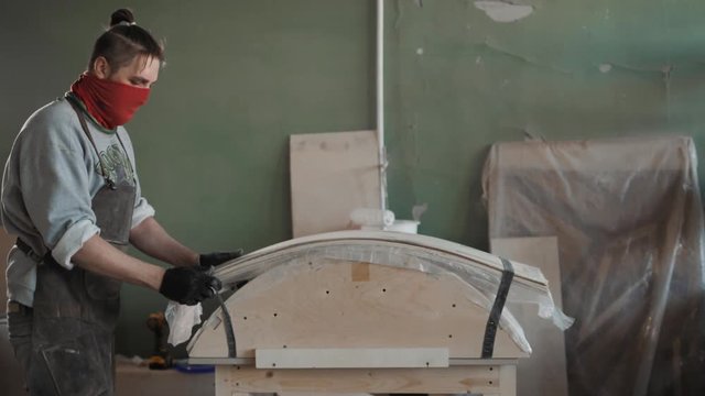 Worker glues veneer on a wooden part apt glue press machine plywood workshop factory. Craftman man equipment