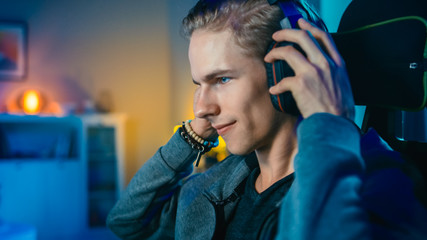 Gamer Puts His Headset with a Mic On and Starts Playing Shooter Online Video Game on His Personal Computer. Room and PC have Colorful Neon Led Lights. Cozy Evening at Home. © Gorodenkoff