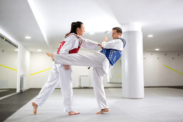 Two taekwondists exchanging punches and kicks in training wearing protective gear