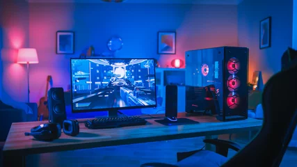 Fototapete Gaming Powerful Personal Computer Gamer Rig with First-Person Shooter Game on Screen. Monitor Stands on the Table at Home. Cozy Room with Modern Design is Lit with Pink Neon Light.  © Gorodenkoff