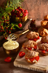 Eclairs custard cakes (shu, profiteroles) with strawberries on a dark background. Still life.