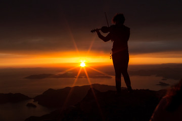 Silhouette of a woman with a violin at sunset on top of the mountain