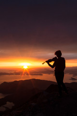 Silhouette of a woman with a violin at sunset on top of the mountain