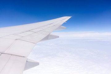 Wing of airplane flying above the clouds in the sky background.