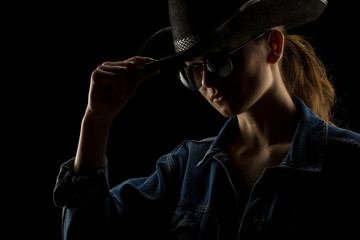 Silhouette of young unknown woman with kowboy hat and sunglasses on black background