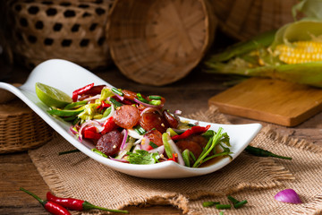 Spicy Chinese pork sausage with vegetable Thai salad in white plate on wood background