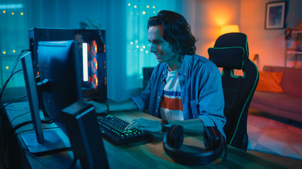 Excited Gamer Playing Online Video Game on His Personal Computer. Room and Personal Computer have...