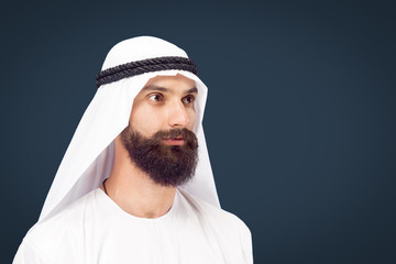 Half-length portrait of arabian saudi businessman on dark blue studio background. Young male model posing and looking serious and calm. Concept of business, finance, facial expression, human emotions.