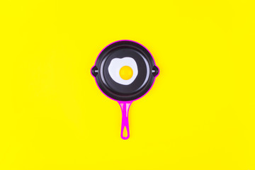 Fried eggs on pink frying pan over yellow background. Top view. Flat lay. Minimal style.