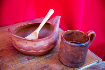 Wooden bowl mug spoon mahogany painted with a simple pattern on a red background. Selective focus. Folk wooden art. Leisure Hobbies.