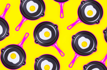 Creative food pattern with fried eggs on pink pans over yellow background. Top view. Creative...