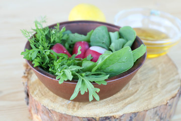 radish salad with green dill, cress salad and arugula leaves in a clay bowl with lemon and olive oil on a wooden board