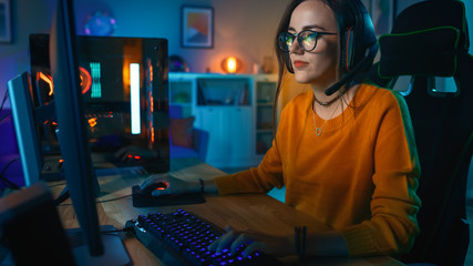 Excited and Concentrated Gamer Girl in Glasses and Headset with a Mic Playing Online Strategy Video Game on Her Personal Computer. Room and PC have Colorful Warm Neon Led Lights. Cozy Evening at Home. © Gorodenkoff