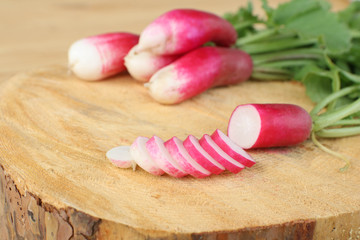 thin radish slices on wooden cutting board with bunch of radish