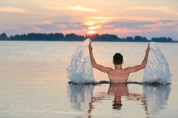 a boy in a river spreads his arms to the side and splashes water