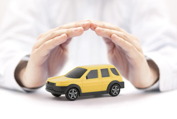 Car insurance concept with yellow car toy covered by hands