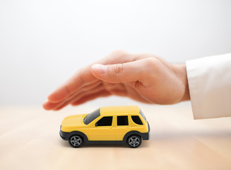 Car insurance concept with yellow car toy covered by hand 