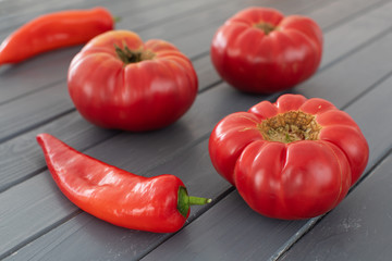 Pink bulgarian tomatoes and sweet red peppers on a gray wooden table, close up