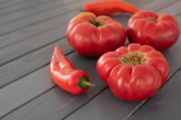 Three pink bulgarian tomatoes and two sweet red peppers on a gray wooden table, close up