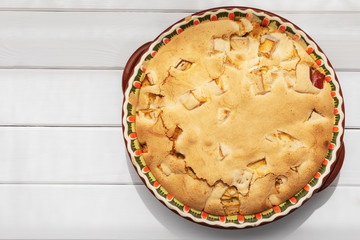 Apple pie with crispy crust in round baking dish on white wooden table, top view with copy space