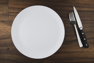 Empty white plate, spoon and knife isolated on wooden background. diet concept.