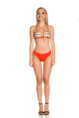 Pretty young smiling lady in red bikini swimsuit and sandals on white background