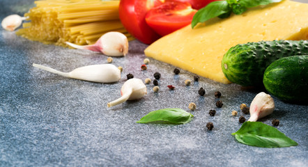 Italian ingredients of pasta and vegetables tomatoes, pasta, garlic, pepper, cheese, spices on a gray background.