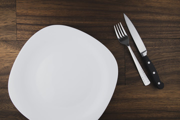 Empty white plate, spoon and knife isolated on wooden background. diet concept.