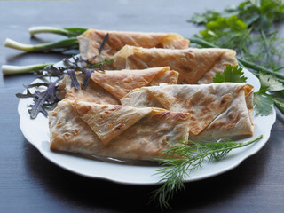Fried bread rolls lavash filled with herbs and cheese in a white plate on a dark table.