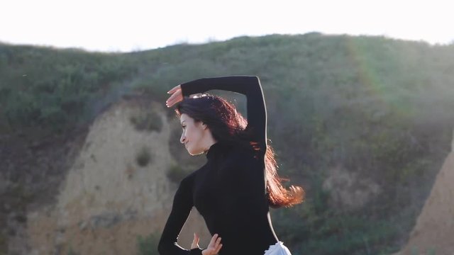 pretty smiling brunette with long loose hair dances on evening sea beach against hills at sunset closeup slow motion