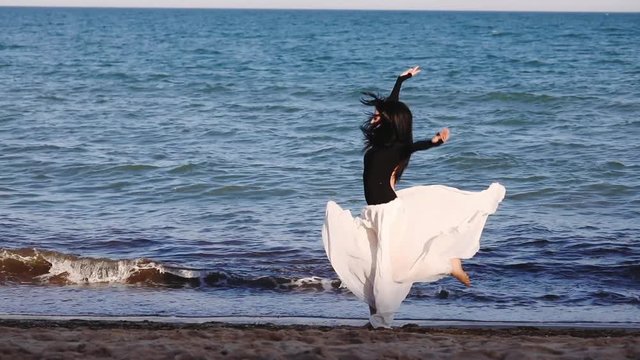 graceful long haired girl in loose chiffon skirt runs and jumps with twine on evening sea coast slow motion