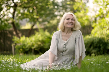 Senior woman in dress sitting on grass at the park on sunny day