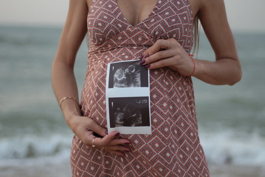 pregnant girl holding ultrasound results in her hands against the background of the sea