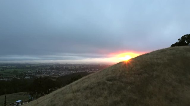 Aerial flyover of grassy ridge revealing a beautiful sunset over the rebuilding Santa Rosa, California after the 2017 Tubbs wildfire.