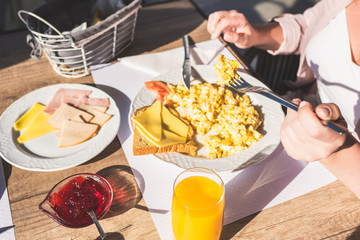 Woman have a breakfast with scrambled eggs, fresh orange  juice ham, cheese, bread and jam in a hotel restaurant.