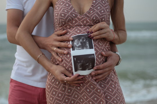 pregnant girl holding ultrasound results in her hands against the background of the sea