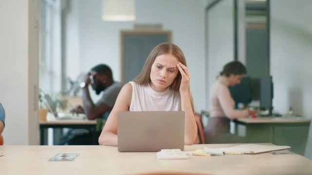 Young woman receiving bad letter on laptop in office. Sad freelance woman